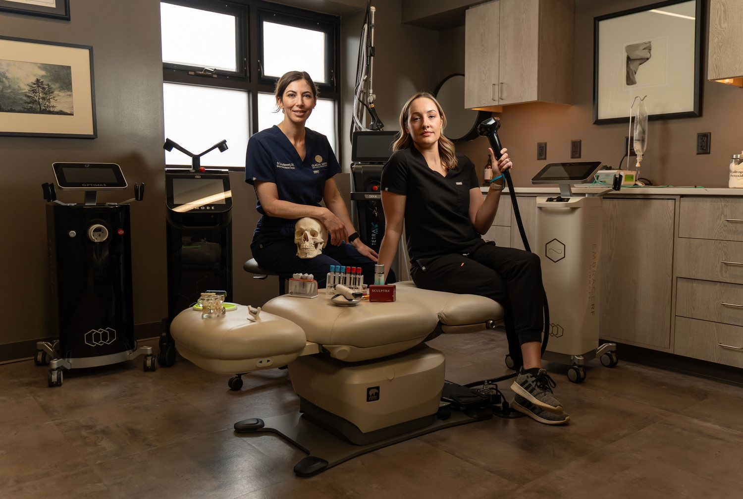 Inside a Refined treatment room, with team members seated beside the treatment chair and laser equipment