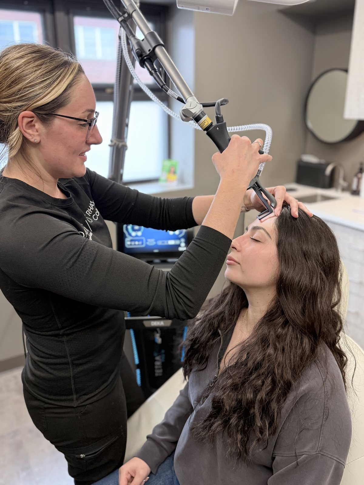 A CO2 laser treatment in progress at Refined, with the provider guiding the handpiece over the patient's forehead